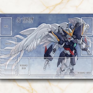 May include: A rectangular Gundam card game playmat featuring a detailed illustration of a Gundam robot with large white wings. The mat has designated areas for game components and the text "Gundam Card Game".