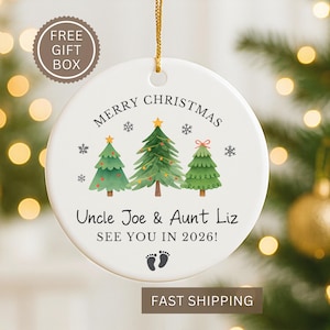 May include: A white ceramic Christmas ornament with a gold string. The ornament features three green Christmas trees, snowflakes, and the text "MERRY CHRISTMAS" and "Uncle Joe & Aunt Liz SEE YOU IN 2026!".