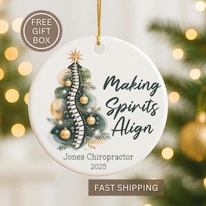 May include: A white ceramic Christmas ornament with a gold string. The ornament features a Christmas tree design with a spine in the center, gold ornaments, and the text "Making Spirits Align." It also includes the text "Jones Chiropractor 2025."