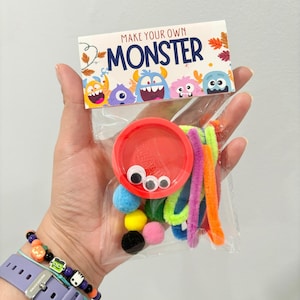May include: A clear plastic bag containing a red lid with googly eyes, colorful pom-poms, and pipe cleaners. The bag is labeled "MAKE YOUR OWN MONSTER" with cartoon monster illustrations.