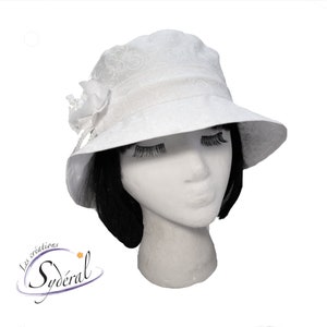 Peut inclure: Chapeau blanc en forme de seau avec un motif floral et une fleur blanche en guise d'ornement. Le chapeau est fait d'un tissu doux et léger et a une large bordure.