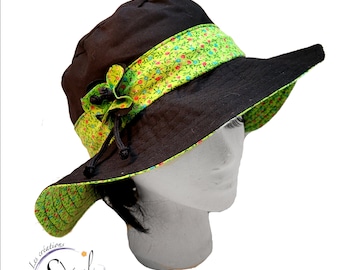 Puede incluir: Un sombrero de sol negro y verde con una banda de estampado floral. El sombrero tiene un ala ancha y un adorno floral en el lateral.