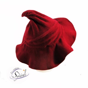 May include: A deep red felt witch hat with a pointed crown and a wide brim. The hat is made of soft, plush fabric and has a slightly ruffled edge.
