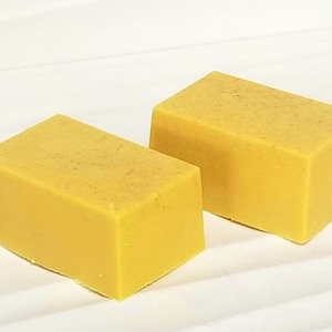 Puede incluir: Dos barras rectangulares de jabón amarillo. El jabón es de color amarillo brillante y tiene una superficie ligeramente texturizada.