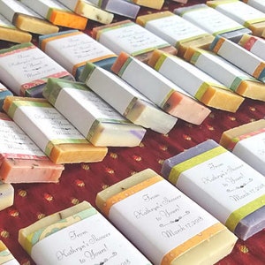 May include: An assortment of colorful, rectangular soaps, each wrapped with a white label and decorative band. The soaps are various colors, including yellow, orange, pink, green, and purple. The labels read "From Kathryn's Shower to Yours! March 17, 2018."