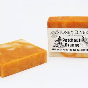 May include: Two bars of handmade soap. One bar is a rectangular shape with orange and white swirls. The other bar is rectangular with a label that reads "Stoney River Patchouli Orange Real Soap Made the Old-Fashioned Way."