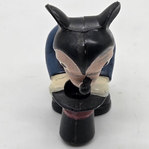 May include: A vintage fox figurine dressed as a magician, wearing a black top hat with a red band. The fox has black ears and a black face with a pink nose and cheeks. It is wearing a blue jacket and white trousers.