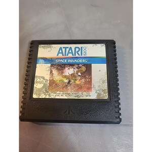 May include: A black Atari 5200 video game cartridge for the game Space Invaders. The label features the Atari logo, the text Space Invaders, and a colorful graphic illustration. The plastic casing has a textured border and the Atari logo embossed.