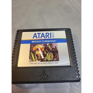 May include: A black Atari 5200 video game cartridge for Missile Command. The label features the Atari logo, the text Missile Command, and an illustration of a military figure with a missile launch. The bottom of the cartridge has the Atari logo.