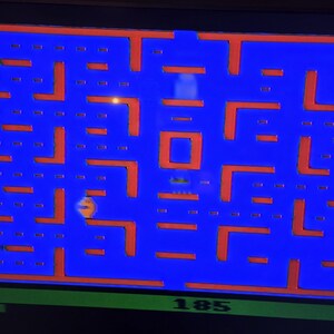 May include: A screenshot of the classic arcade game Pac-Man. The game features a blue maze with orange walls and a yellow Pac-Man character. The score of 185 is displayed at the bottom of the screen.