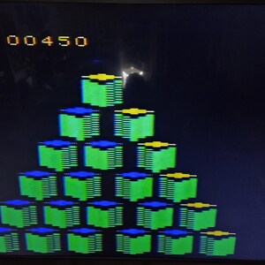 May include: A screenshot of a retro video game with a pyramid of green, blue, and yellow blocks. The score "00450" is displayed at the top of the screen. The background is black.