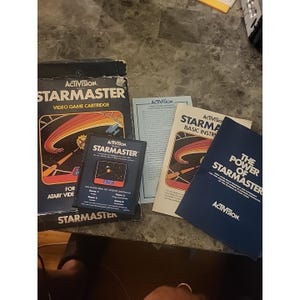 May include: Activision Starmaster video game cartridge for Atari Video Computer System, including the original cardboard box, a basic instruction manual, a warranty card, and a blue booklet titled The Power of Starmaster with white text.