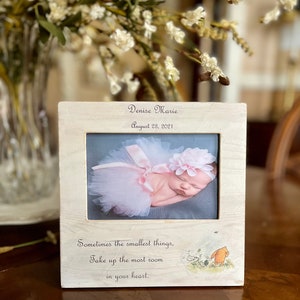 May include: A white wooden picture frame with a photo of a baby girl wearing a pink tutu and a flower headband. The frame has the text "Denise Marie" and "August 23, 2021" engraved on it. The quote "Sometimes the smallest things, take up the most room in your heart." is printed below the photo. A Winnie the Pooh illustration is in the bottom right corner.