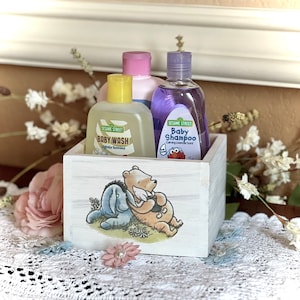 May include: White wooden box with a Winnie the Pooh and Eeyore design. The box contains three bottles of baby wash and shampoo. The bottles are labeled "Sesame Street Baby Wash" and "Sesame Street Baby Shampoo".