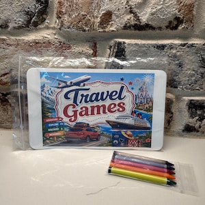 May include: A rectangular card in a clear plastic sleeve featuring the text Travel Games, an airplane, a cruise ship, a car, and a castle. Below the card is a small clear plastic bag containing five wax crayons in yellow, orange, pink, purple, and black.
