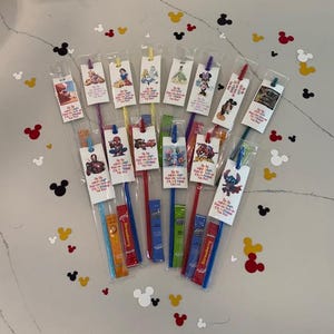 May include: A collection of colorful bookmarks featuring various cartoon characters, each packaged with a straw. The bookmarks have different colored straws and are packaged in clear plastic. Mickey Mouse confetti is scattered around the bookmarks.