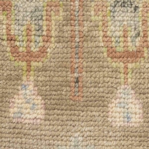 May include: Close-up of a beige rug with a repeating pattern. The design features geometric shapes in shades of brown, pink, green, and blue. The rug has a textured surface.