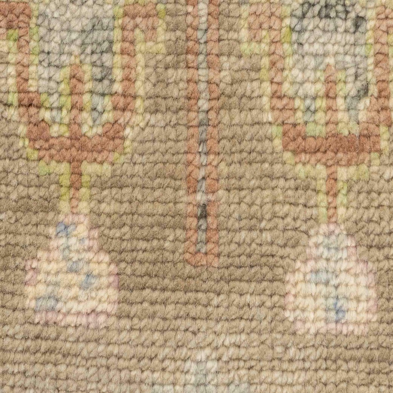 May include: Close-up of a beige rug with a repeating pattern. The design features geometric shapes in shades of brown, pink, green, and blue. The rug has a textured surface.