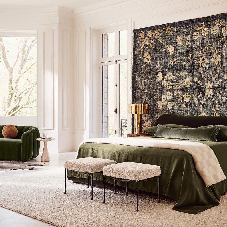 Puede incluir: Un dormitorio lujoso con una colcha de terciopelo verde oscuro, almohadas a juego y una manta color crema. Dos taburetes tapizados con patas de metal negro est&aacute;n al pie de la cama. Una gran tapicer&iacute;a floral cuelga sobre la cama.