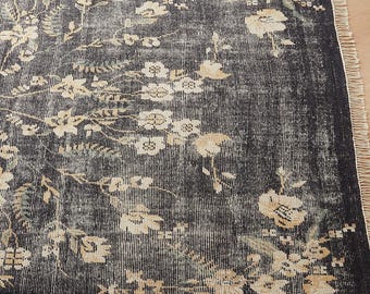 May include: A distressed rug featuring a dark grey backdrop and a floral design in cream and light green. The rug has a fringed edge and a vintage aesthetic, suitable for living rooms or bedrooms.