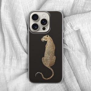 May include: A black phone case featuring a detailed illustration of a leopard. The leopard is depicted in a seated position with its tail curled, showcasing its distinctive spotted coat. The case has a clear border.
