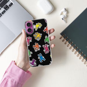 May include: A black phone case featuring a repeating pattern of colorful, stylized figures in various poses. The figures are outlined in black and filled with bright colors like yellow, red, and blue. The case is held in a person's hand.