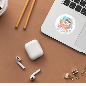 Op de afbeelding: Een ronde sticker met een witte konijn met een zwarte zonnebril, ontspannend in een roze donut-zwemband terwijl het een geel drankje vasthoudt. De tekst "TOO SWEET TO STRESS" staat in lichtblauw onder het konijn op een lichtblauwe achtergrond.