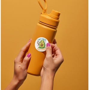 Op de afbeelding: Een matte mosterdgele waterfles met een schroefdop en een draaglus. In het midden is een ronde sticker aangebracht met een cartoon avocado die een gezichtsmasker draagt en een spiegel vasthoudt, met de tekst CAN'T TALK SELF-CARING.