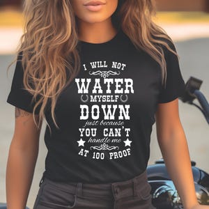 Puede incluir: Camiseta negra con texto blanco: "I WILL NOT WATER MYSELF DOWN just because YOU CAN'T handle me AT 100 PROOF." La camiseta es de manga corta y tiene cuello redondo. El texto está en negrita y estilizado.