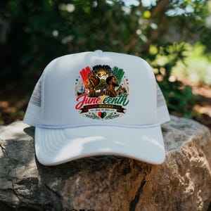 May include: White trucker hat with a mesh back and a curved brim. The front of the hat features a colorful graphic with the words "Juneteenth" and "Freedom, Resilience, Joy" with a date. The design includes images of people and flags.