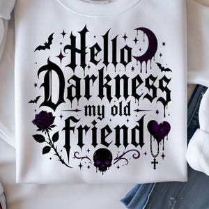 May include: A white sweatshirt featuring a black and purple graphic print with the text Hello Darkness my old friend. The design includes a crescent moon, bats, a rose, a skull, and a broken heart with a cross pendant, all in a gothic font.