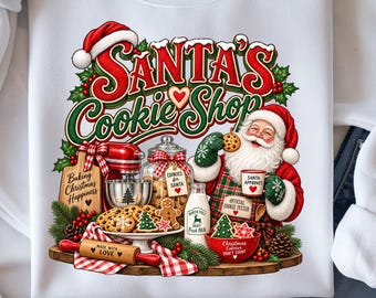 Może przedstawiać: Biała bluza z grafiką Świętego Mikołaja w kuchni oraz napisem Santa's Cookie Shop. Wzór zawiera ciasteczka, wałek do ciasta z napisem Made With Love, butelkę mleka, mikser oraz tabliczki z napisami dotyczącymi świątecznego pieczenia.