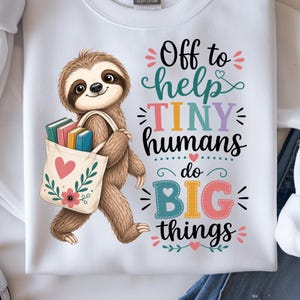 May include: White sweatshirt featuring a smiling sloth carrying a tote bag filled with books. The tote bag has a heart and floral design. Text on the shirt reads "Off to help TINY humans do BIG things" in colorful lettering.