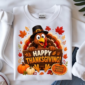 May include: A white crewneck sweatshirt featuring a graphic of a turkey wearing a black pilgrim hat, holding a wooden sign that reads HAPPY THANKSGIVING!. The design includes orange pumpkins, red and orange autumn leaves, and a small sign saying THANKFUL GRATEFUL BLESSED.