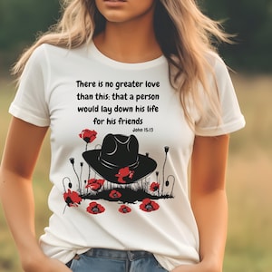 May include: White t-shirt featuring a graphic design with a black hat, red poppies, and the text "There is no greater love than this: that a person would lay down his life for his friends John 15:13."