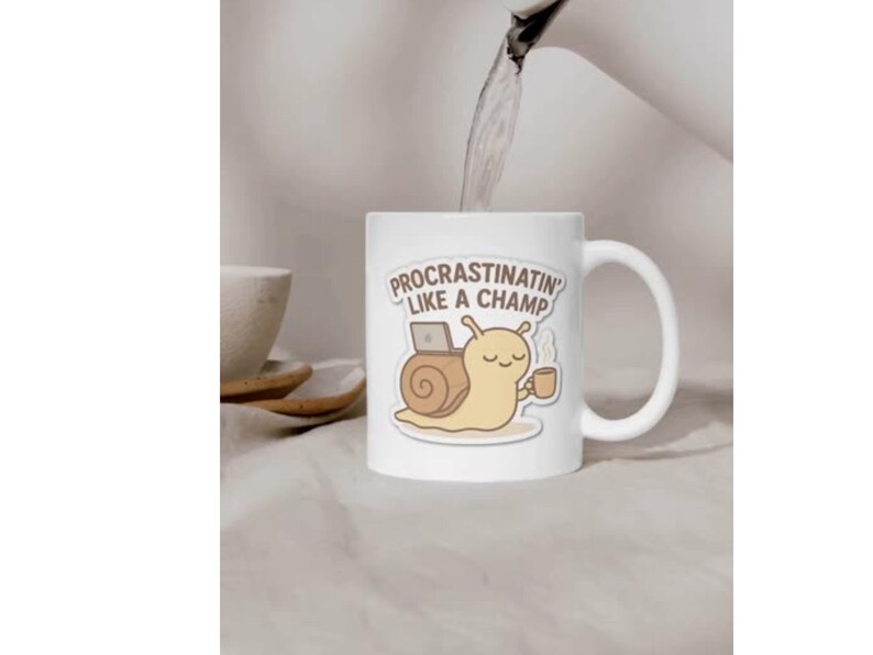 Op de afbeelding: Een witte keramische mok met een cartoonillustratie van een lichtbruine slak met een huisje, die een klein bruin kopje vasthoudt en naast een laptop zit. De tekst boven de slak luidt "PROCRASTINATIN' LIKE A CHAMP" in bruine hoofdletters.