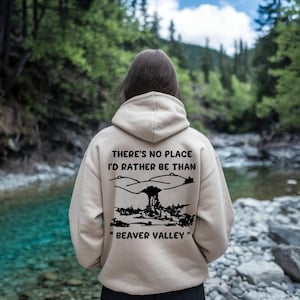 May include: Beige hoodie with a black graphic on the back. The graphic includes the text "THERE'S NO PLACE I'D RATHER BE THAN" above a landscape illustration and the text "BEAVER VALLEY" below it. The hoodie has a hood and a front pocket.