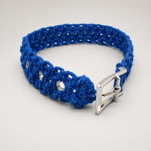 May include: A vibrant blue crochet collar with a silver-colored metal buckle. The collar features a textured, woven design with evenly spaced eyelets. The buckle is rectangular and securely fastens the collar.