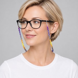 May include: Black-framed eyeglasses featuring a multi-colored beaded chain. The chain consists of small, vibrant beads in a gradient pattern transitioning from purple and blue to green, yellow, and orange, attached to the temples with clear loops.
