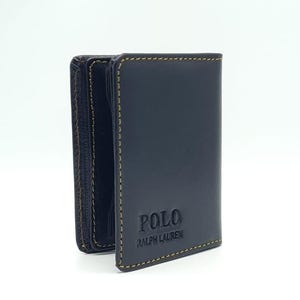May include: A navy blue leather wallet with the embossed text "POLO RALPH LAUREN". The wallet has a bi-fold design with tan stitching. The wallet is set against a white background.