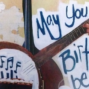 Pu&ograve; includere: Un biglietto di auguri di compleanno con sfondo bianco e lettere blu che dicono "May your birthday be". Si vede una chitarra e un banjo sullo sfondo.