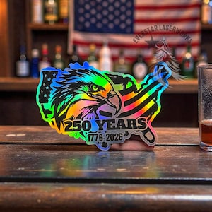 May include: A holographic sticker in the shape of the United States, featuring an eagle head, American flag stripes, and the text "250 YEARS 1776-2026". The sticker has a rainbow color effect.