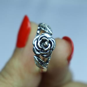 May include: A silver ring with a rose design. The ring features a detailed rose at the centre, with two leaves on either side. This elegant piece of jewellery is suitable for everyday wear or special events.