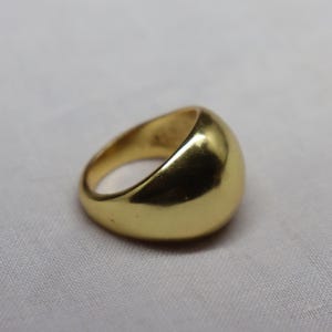 May include: A solid gold-toned ring with a smooth, polished, and rounded dome-shaped surface. The band features a thick, continuous design with a high-shine metallic finish that reflects light across its curved, convex exterior profile.