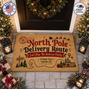 Op de afbeelding: Een rechthoekige, lichtbruine deurmat met de tekst North Pole Delivery Route en Last Stop: The Anderson Family, 24 Maple Street, Columbus, OH. Het ontwerp bevat een silhouet van een kerstman-slee, een huis, dennenbomen en een North Pole-bord.