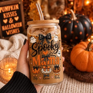 May include: A clear glass tumbler with a bamboo lid and glass straw, featuring a Halloween-themed design with the text Spooky Mama, ghosts, pumpkins, and black bows. The names Lily, Owen, and Ruby are printed at the bottom of the glass.