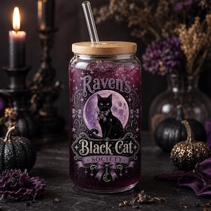 Op de afbeelding: Een doorzichtig glas met een bamboe deksel en een glazen rietje, gevuld met een paarse vloeistof. Het glas is voorzien van een afbeelding van een zwarte kat voor een paarse maan, met de tekst Raven's Black Cat SOCIETY in het wit.