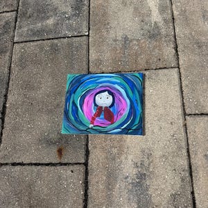 May include: A rectangular painting featuring a cartoon character in a red jacket and black pants, surrounded by swirling blue, teal, and pink colors. The artwork is set against a gray, textured surface.