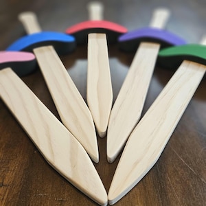 Könnte beinhalten: Eine Sammlung von Holzwerkzeugen mit hellem Holzfinish. Jedes Werkzeug hat eine lange, spitze Klinge und einen farbigen, abgerundeten Kopf in Pink, Blau, Rot, Lila und Grün. Die Werkzeuge sind fächerförmig angeordnet.