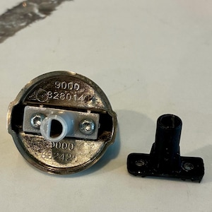 May include: A silver-toned metal knob with a white plastic insert and a separate black plastic piece. The knob has the numbers "9000" and "862425" etched on it.